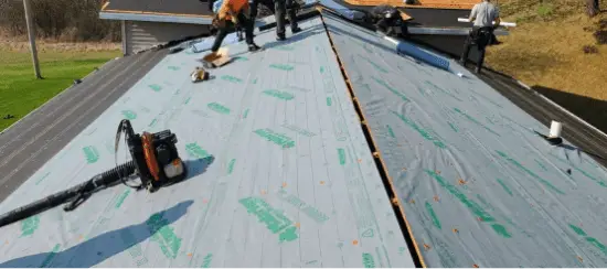 Roofers installing shingles on residential roof with underlayment and tools