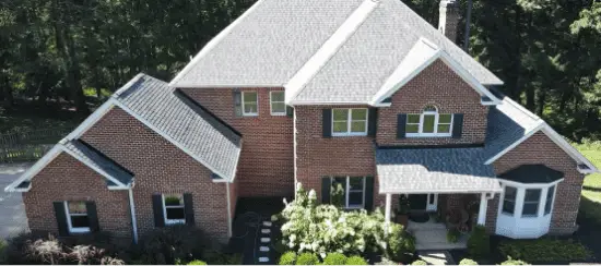 Aerial view of large brick house with attached garage surrounded by trees
