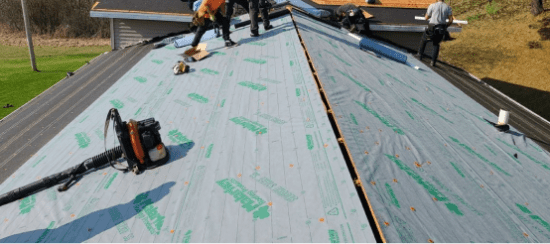Roofers installing shingles on residential roof with underlayment and tools
