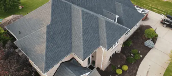 Aerial view of residential house with gray shingle roof and landscaped yard