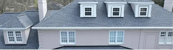 Gray asphalt shingle roof with white dormers and windows on residential house