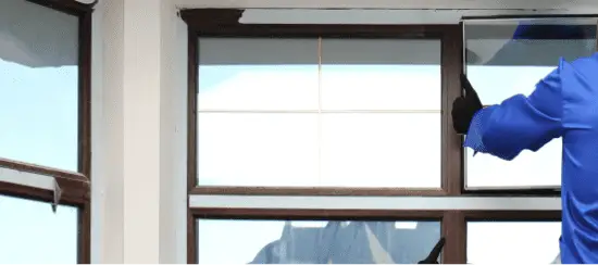 Professional window cleaner in blue uniform cleaning large commercial windows