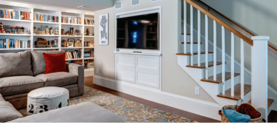 Modern basement living room with built-in bookshelves, TV cabinet, and staircase