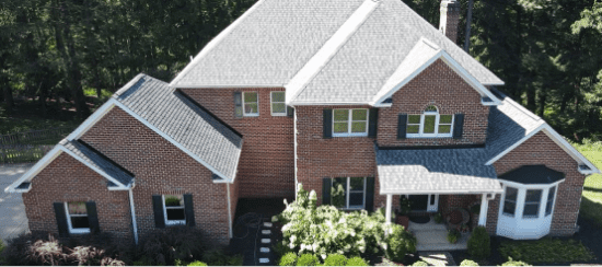 Aerial view of large brick house with attached garage surrounded by trees