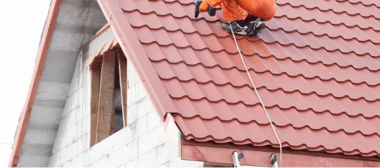 Worker installing red clay roof tiles on residential house with safety equipment