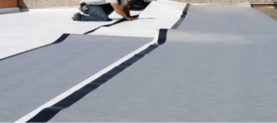 Workers installing white TPO roofing membrane on flat commercial roof surface