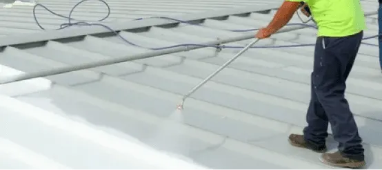 Worker in safety vest applying white coating to commercial roof with spray equipment
