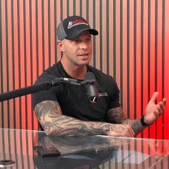 Man with tattoos speaking into a microphone during a podcast interview.