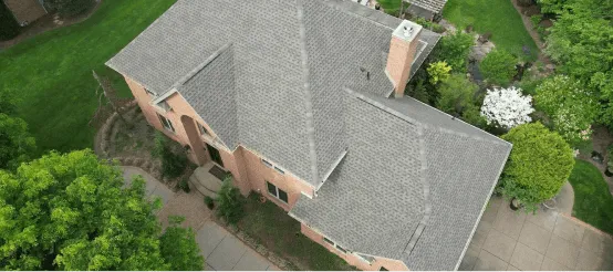 Aerial view of modern brick house with gray shingle roof surrounded by green lawn