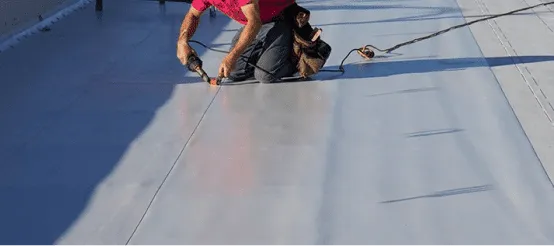 Roofer installing white roofing membrane on commercial flat roof surface