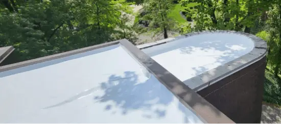 Modern flat roof with white membrane reflecting clouds, surrounded by lush green trees