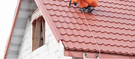 Worker installing red clay roof tiles on residential house with safety equipment