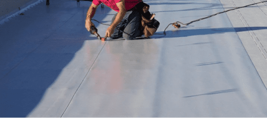 Roofer installing white roofing membrane on commercial flat roof surface