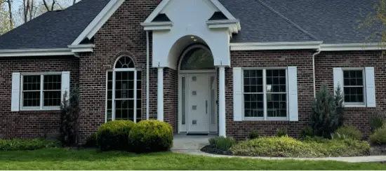 Red brick house with white columns and arched front entrance surrounded by landscaping