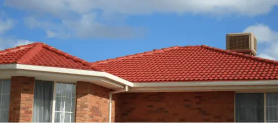 Red tile roof on brick house with blue sky and white clouds background