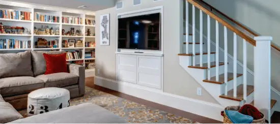 Modern basement living room with built-in bookshelves, TV cabinet, and staircase