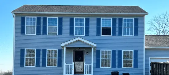 Blue two-story colonial house with white trim and blue shutters on clear day