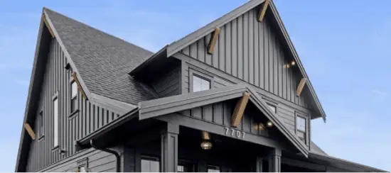 Modern gray vertical siding house with gabled roofs and warm exterior lighting