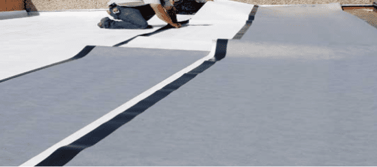 Workers installing white TPO roofing membrane on flat commercial roof surface