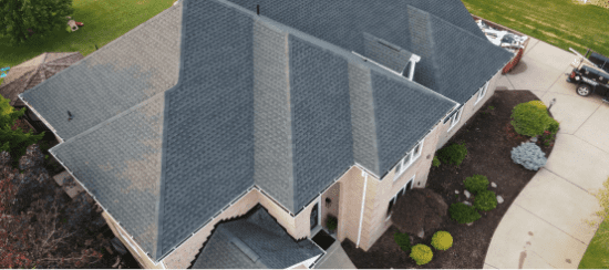 Aerial view of residential house with gray shingle roof and landscaped yard