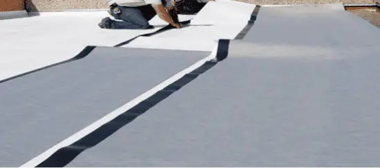 Workers installing white TPO roofing membrane on flat commercial roof surface