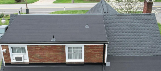 Aerial view of residential house with dark gray shingle roof and brick siding
