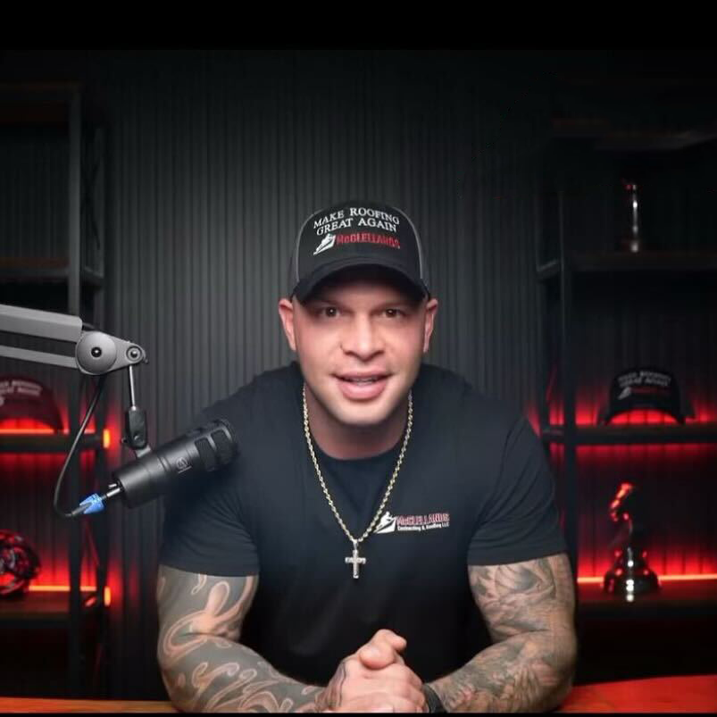 Tattooed man in baseball cap speaking into microphone in podcast studio with red lighting
