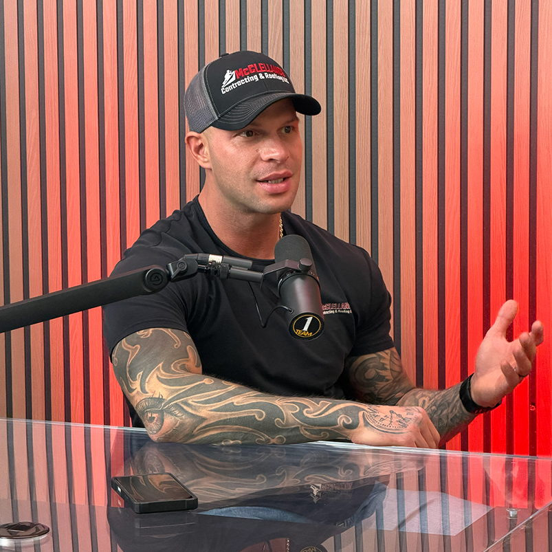 Man with tattoos speaking into a microphone during a podcast interview.