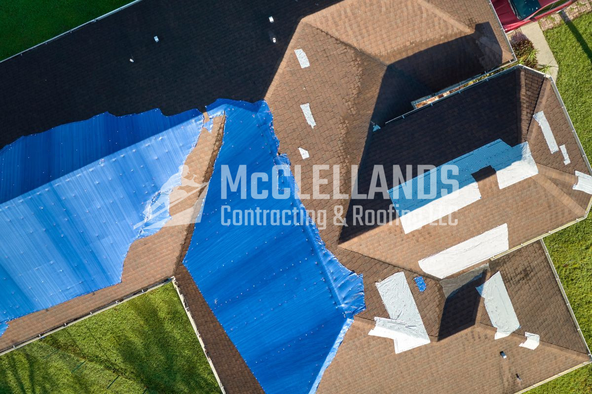 Aerial view of a roof under repair with blue tarps covering damaged sections.