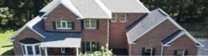 Aerial view of a large brick house with multiple gables and lush surroundings.