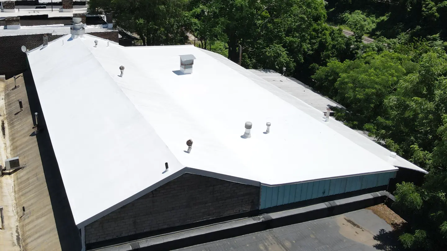 Aerial view of a large building with a bright white rooftop surrounded by trees.