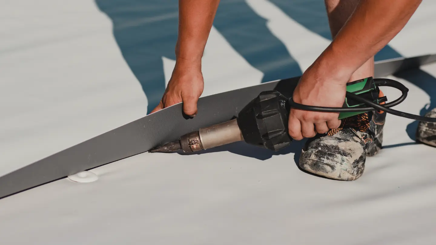 Close-up of a person using a heat gun to seal roofing material.