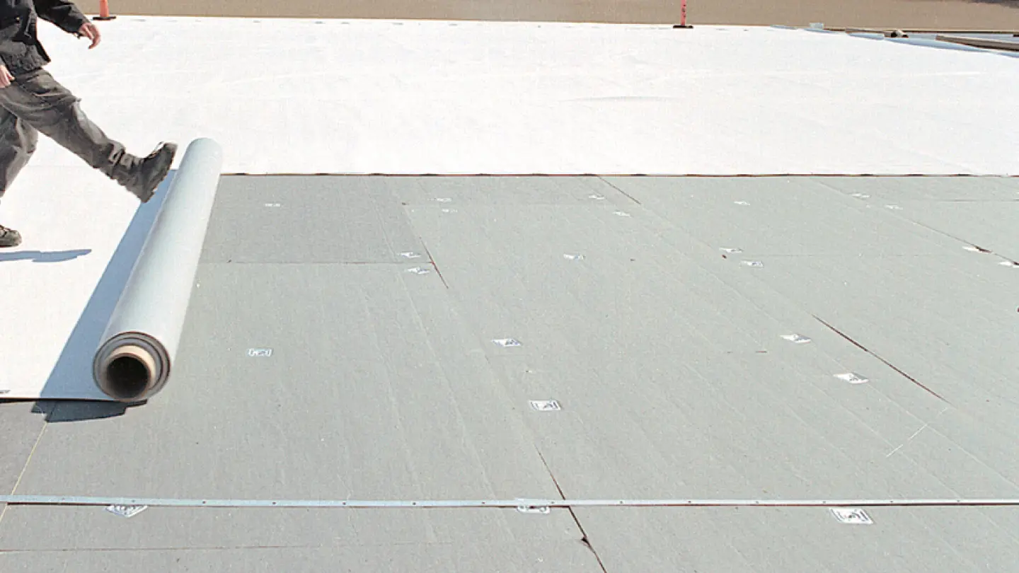 Worker installing roll roofing on flat rooftop for waterproofing.