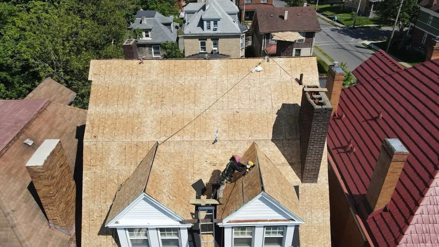 Roofer working on a residential home's plywood roof with nearby chimneys