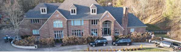 Large brick house with multiple vehicles parked in front.