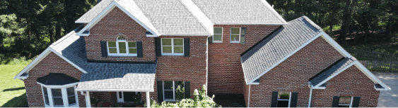 Aerial view of a large brick house with gabled roof and lush surroundings.